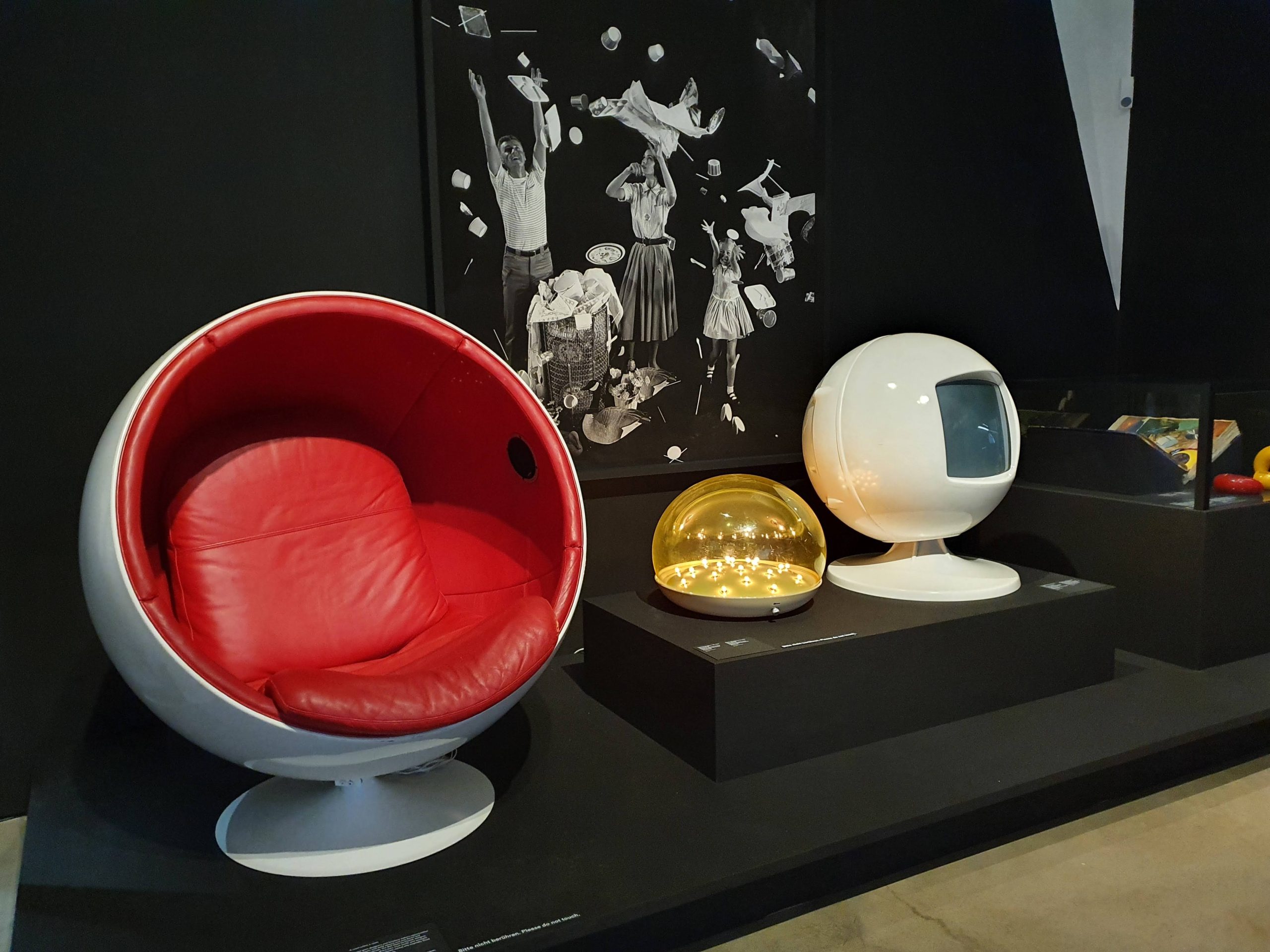 Poltrona a sfera rossa e TV retrò esposti in un museo di design moderno, illuminati e di colore vivace.